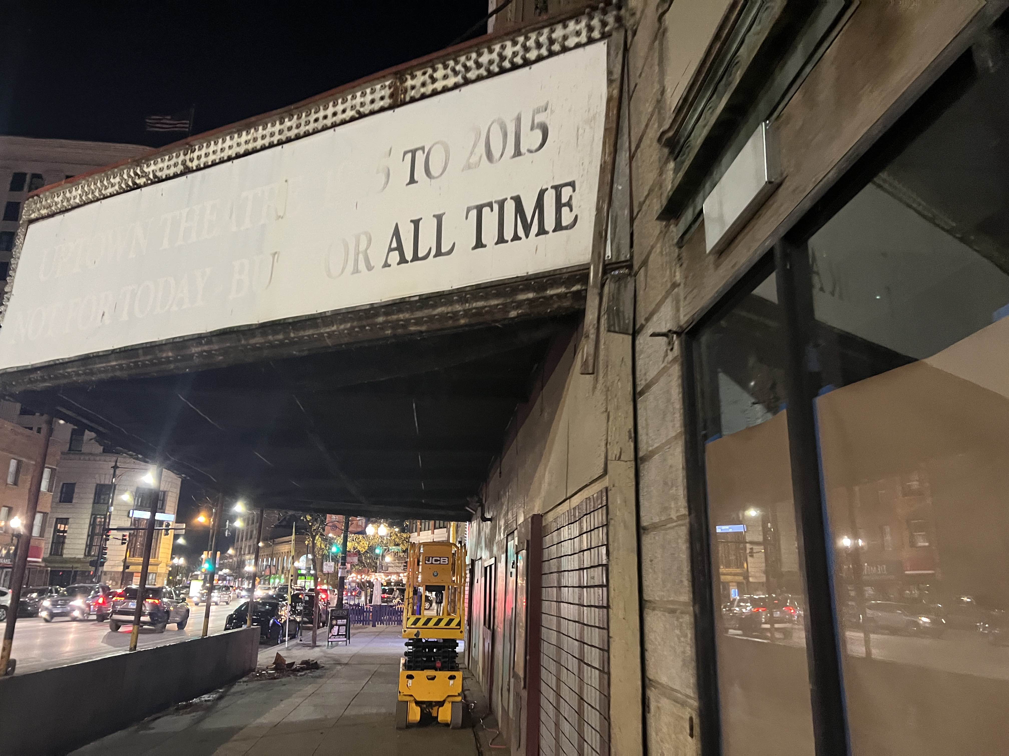 an abadoned theatre's faded marquee- the only words easily legible are 'to 2015' and 'all time'. A colorful city night can be seen in the background.